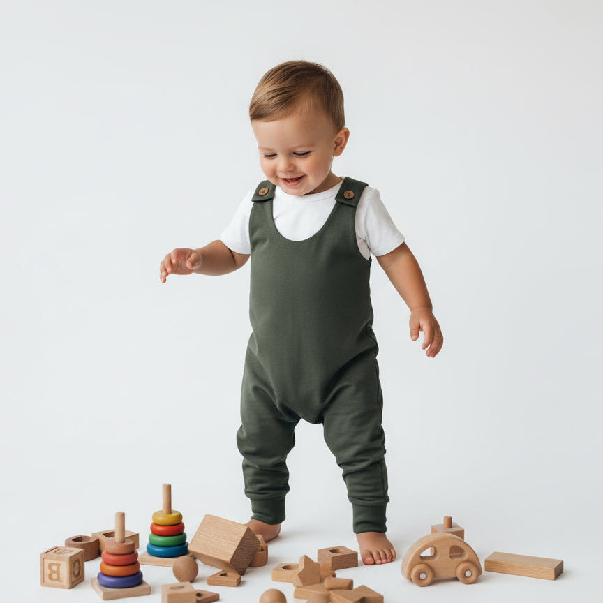 Child in green overalls standing with wooden toys on a white background