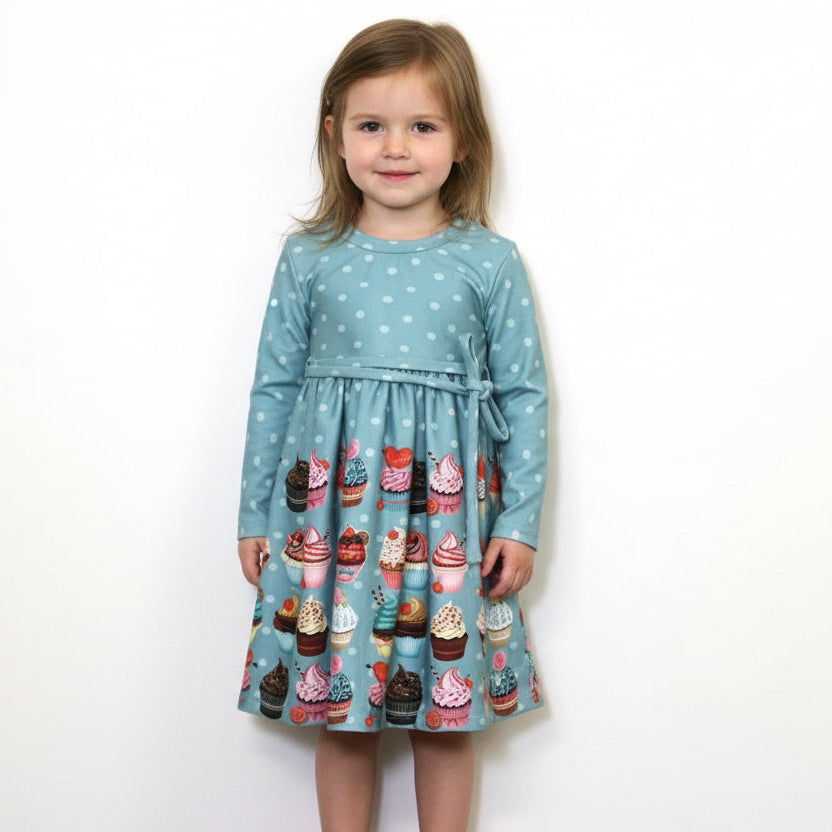Young girl wearing a blue dress with cupcake pattern on a white background