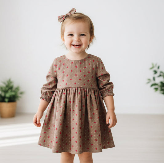 Child wearing a brown dress with a subtle pattern, standing in a bright room with plants.