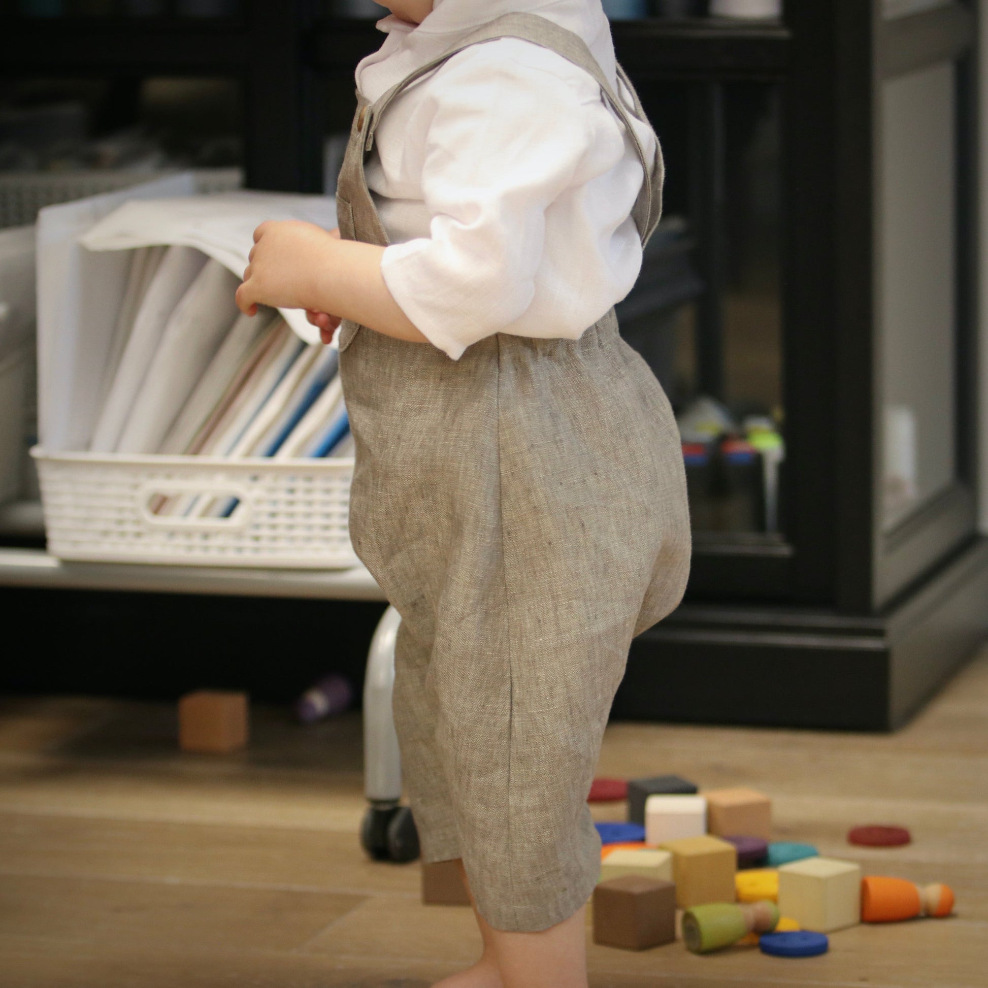 Child in a formal outfit standing on a wooden floor with toys scattered around