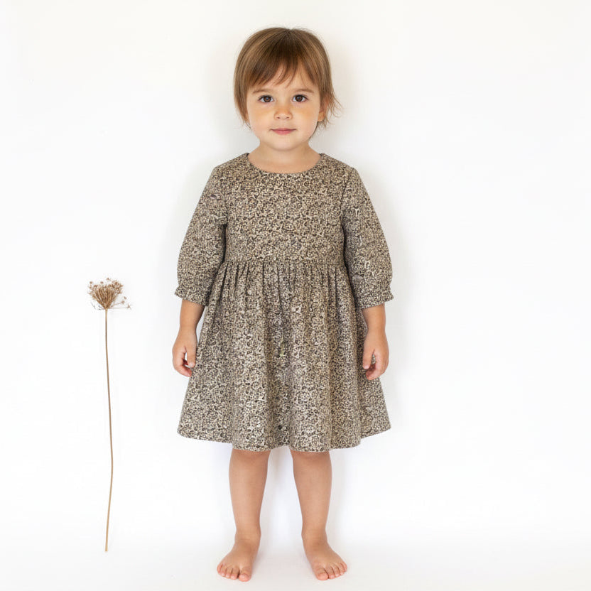 Young child wearing a patterned dress standing on a white background